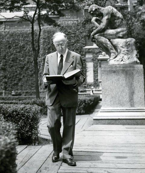 Irwin Edman CC 1916, GSAS 1920 walks on the sidewalk reading a book.